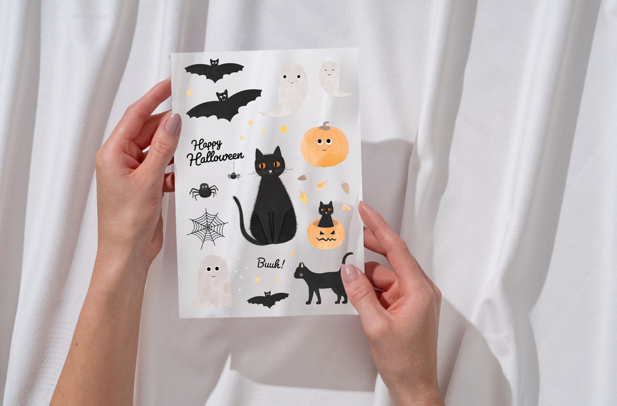 Eine Halloween-Karte mit niedlichen Illustrationen. Zu sehen sind lächelnde Geister, schwarze Katzen, Fledermäuse, Spinnen, ein Spinnennetz und Kürbisse. Der Schriftzug "Happy Halloween" und das Wort "Buuh!" sind ebenfalls enthalten.