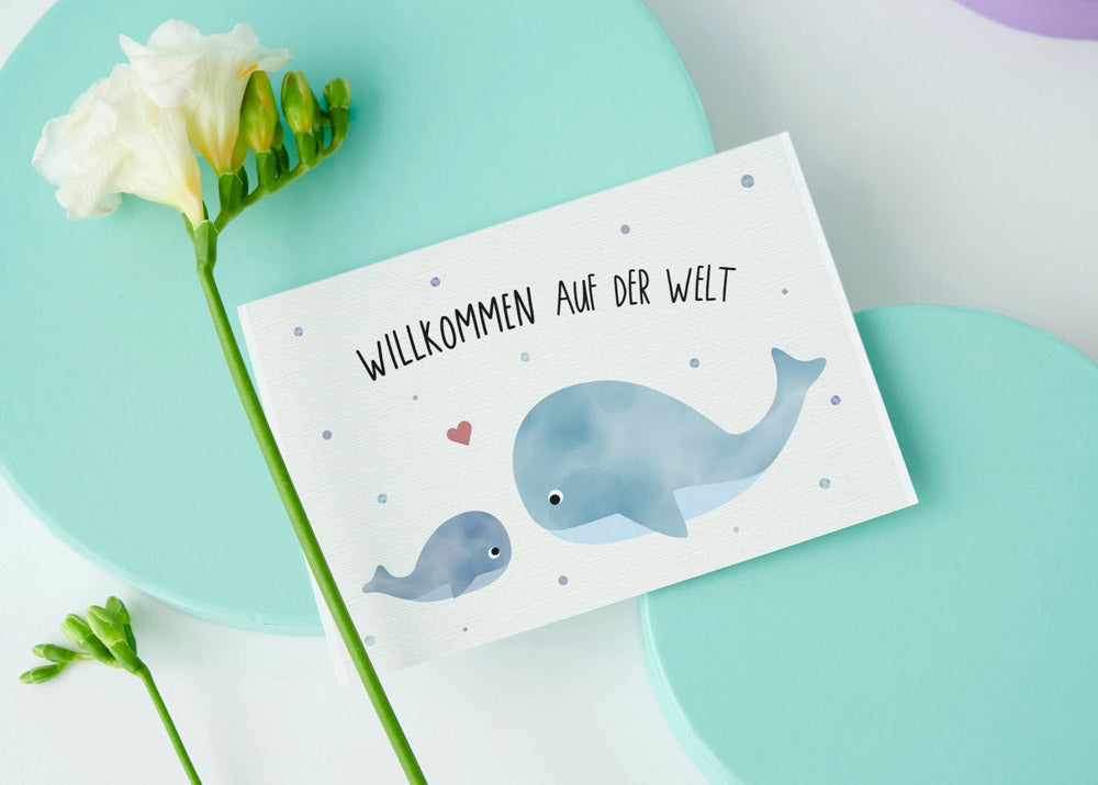 Postkarte mit Wal und dem Schriftzug „Willkommen auf der Welt“ im niedlichen Design, ideal als Geburtskarte oder Willkommensgruß für Babys.