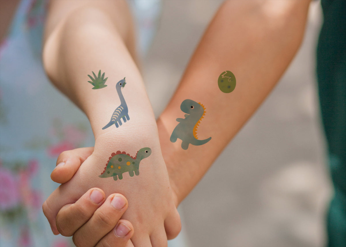 Bogen mit temporären Kindertattoos im Dinosaurier-Design – mit fröhlich illustrierten Dinos wie T-Rex, Triceratops und Stegosaurus. Ein Dino-Spaß für kleine Entdecker:innen