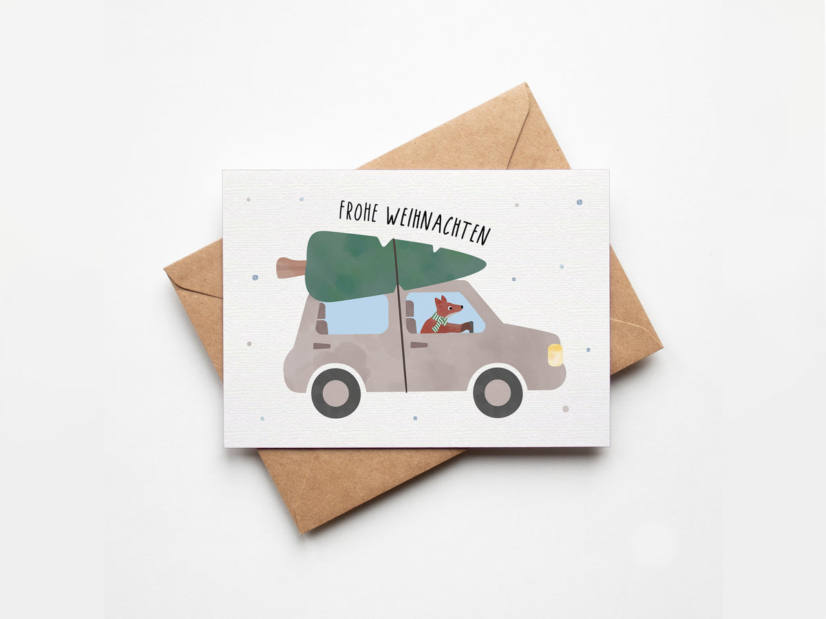 Postkarte mit Fuchs, der ein Auto mit Tannenbaum auf dem Dach fährt, und dem Schriftzug „Frohe Weihnachten“ im verspielten Design, ideal als Weihnachtskarte oder kleiner Gruß.