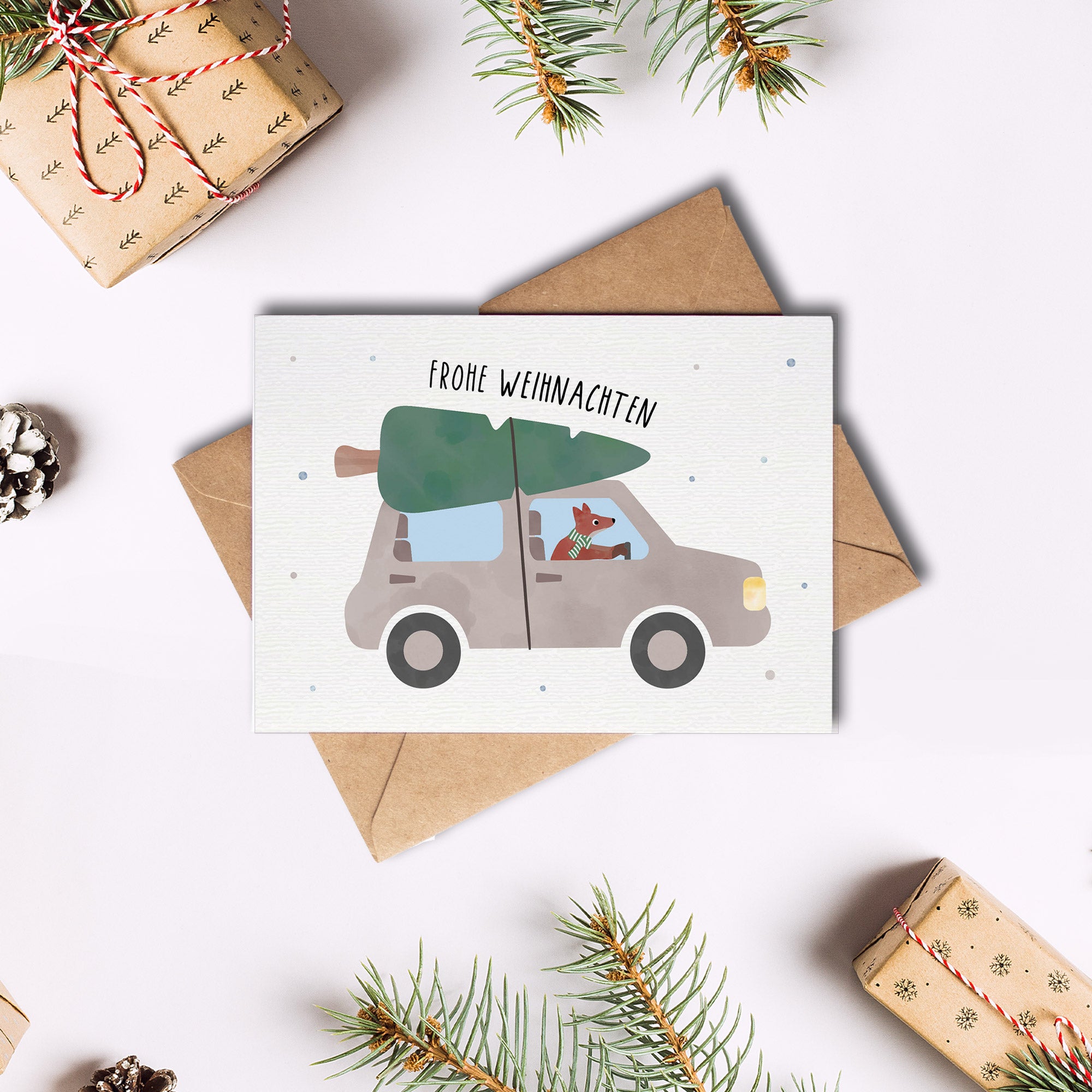 Postkarte mit Fuchs, der ein Auto mit Tannenbaum auf dem Dach fährt, und dem Schriftzug „Frohe Weihnachten“ im verspielten Design, ideal als Weihnachtskarte oder kleiner Gruß.