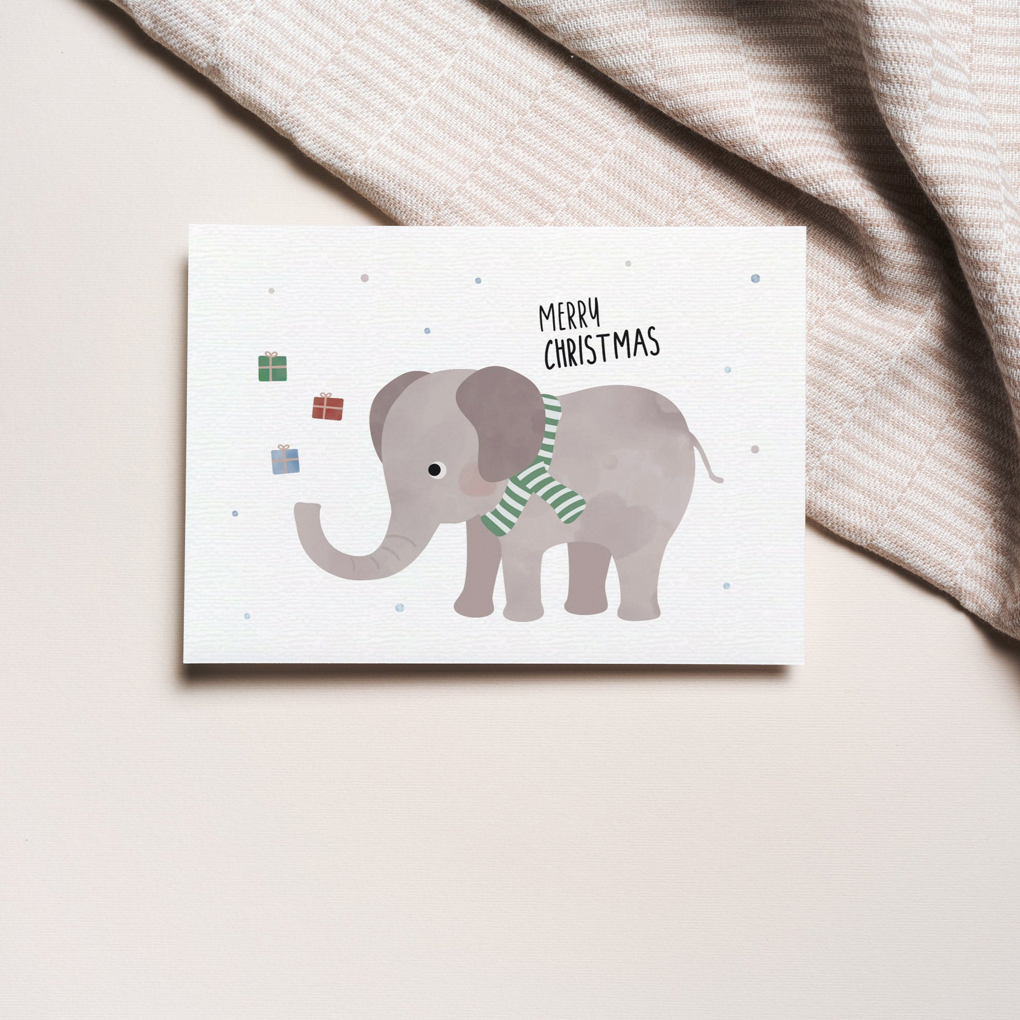 Postkarte mit Elefant mit grünem Schal sowie dem Schriftzug „Frohe Weihnachten“ der Geschenke in die Luft wirft, ideal als Weihnachtskarte oder kleiner Gruß.
