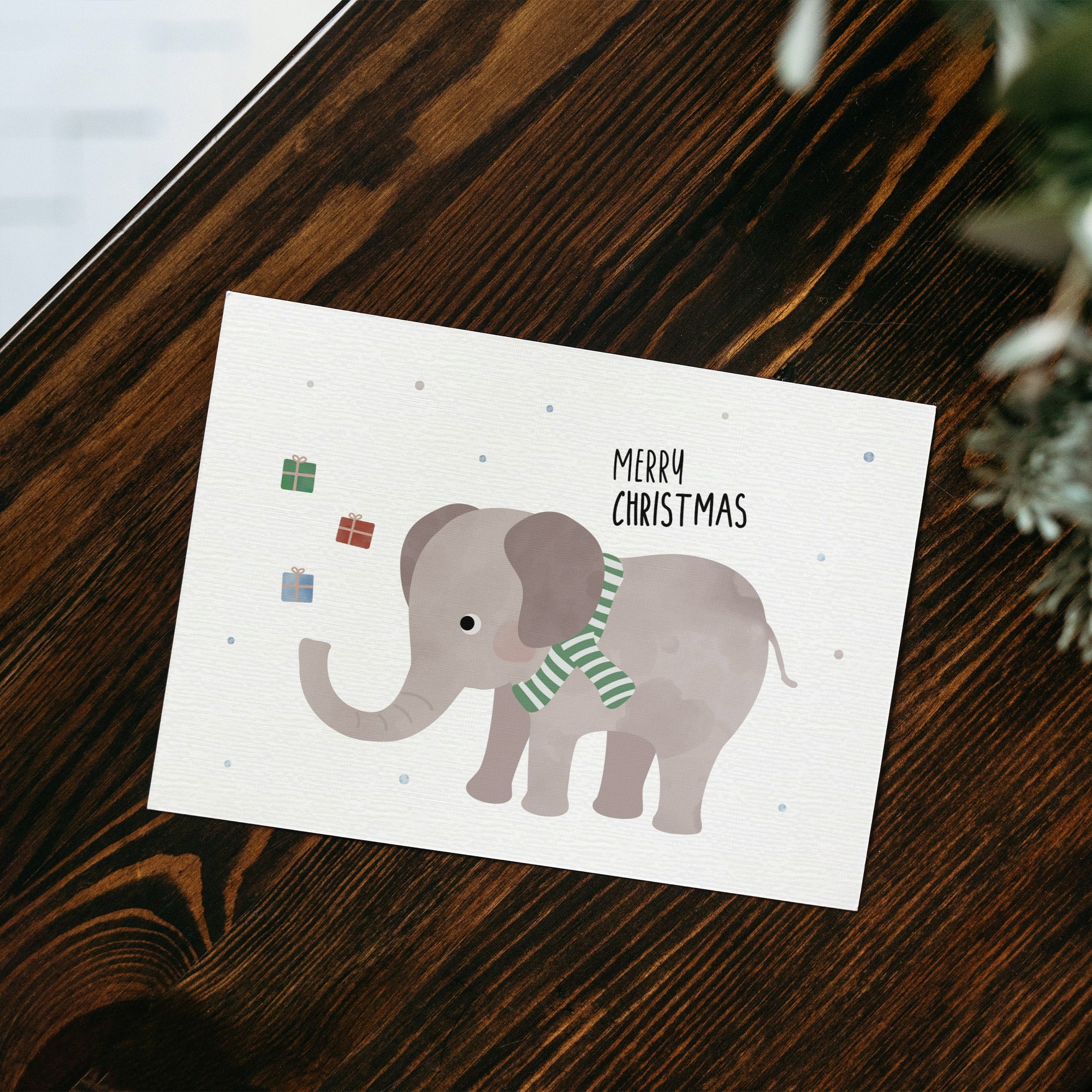 Postkarte mit Elefant mit grünem Schal sowie dem Schriftzug „Frohe Weihnachten“ der Geschenke in die Luft wirft, ideal als Weihnachtskarte oder kleiner Gruß.