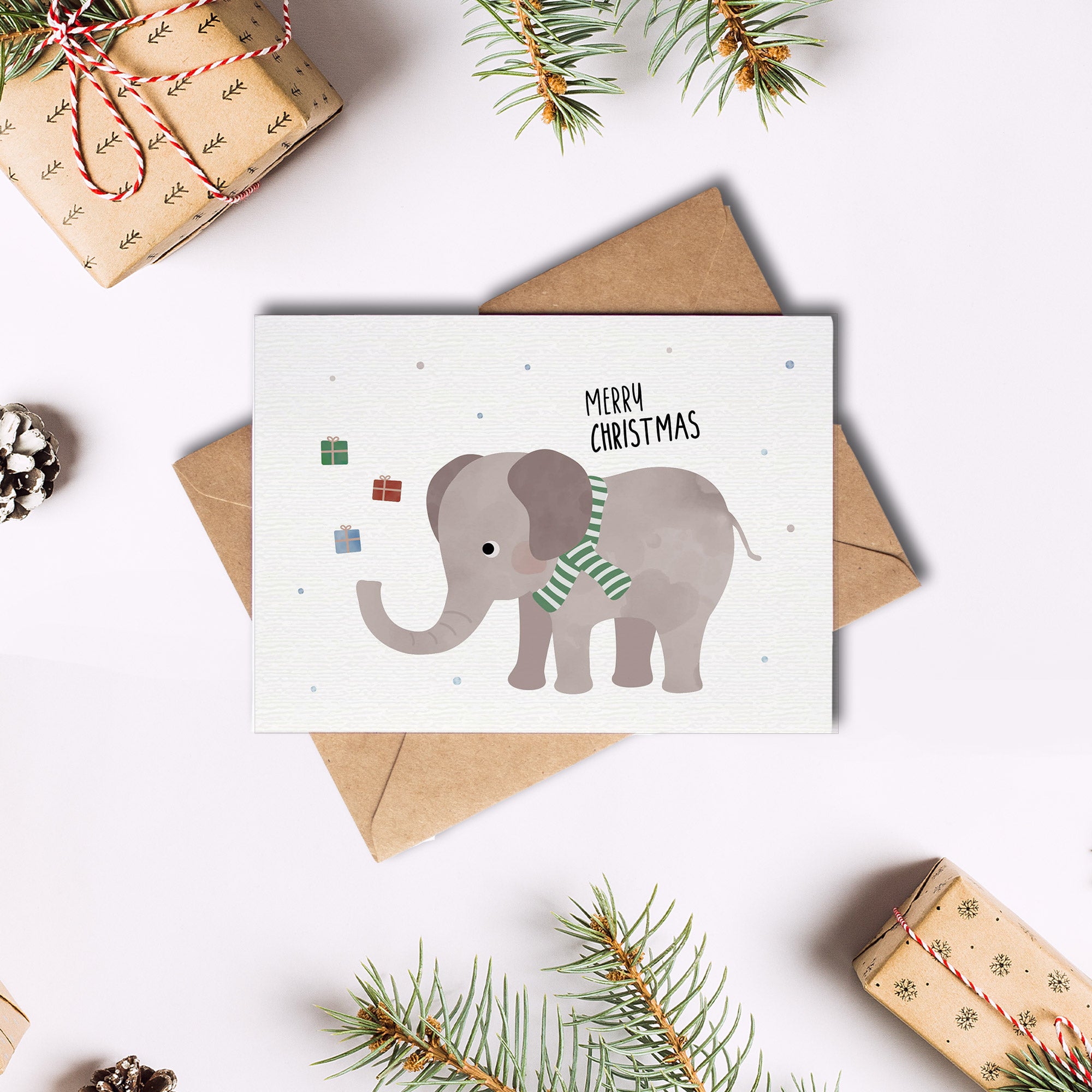 Postkarte mit Elefant mit grünem Schal sowie dem Schriftzug „Frohe Weihnachten“ der Geschenke in die Luft wirft, ideal als Weihnachtskarte oder kleiner Gruß.