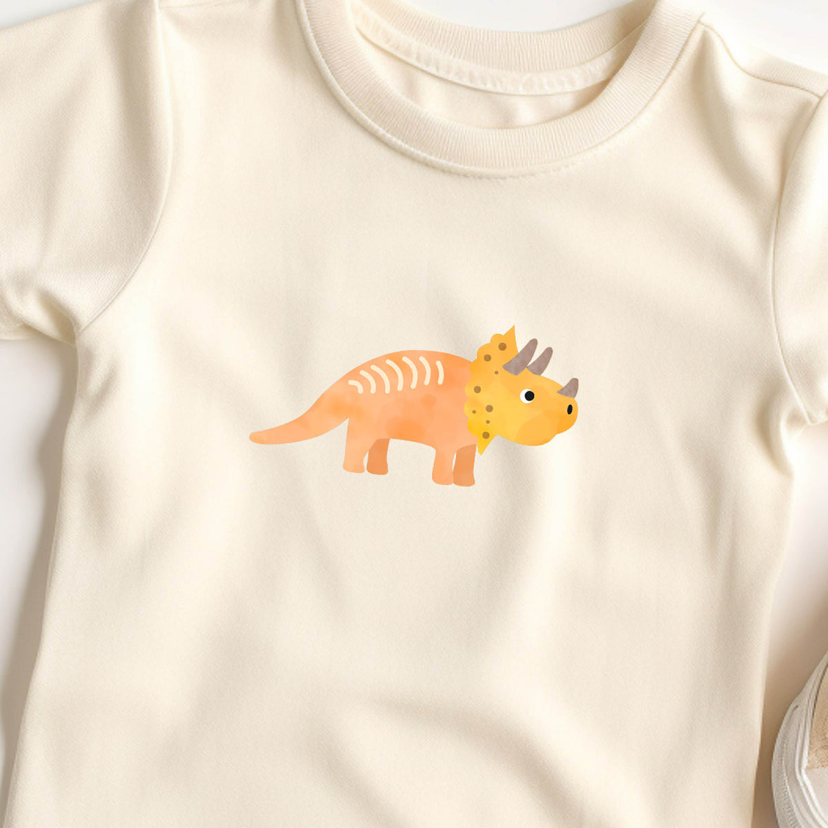 Bügelbild mit orange-gelben Triceratops im kindlichen Design, perfekt zum Aufbügeln auf Kinderkleidung und Accessoires.