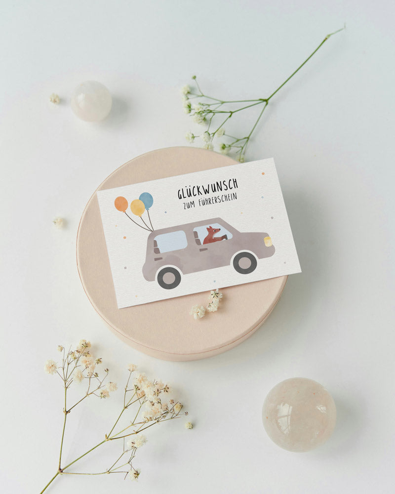 Illustrative Glückwunschkarte zum Führerschein mit Auto, Luftballons und der Aufschrift ‚Glückwunsch zum Führerschein‘ – liebevoll gestaltete Karte von by Clou