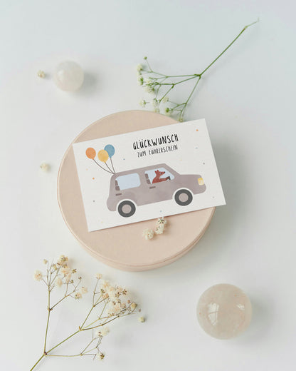 Illustrative Glückwunschkarte zum Führerschein mit Auto, Luftballons und der Aufschrift ‚Glückwunsch zum Führerschein‘ – liebevoll gestaltete Karte von by Clou