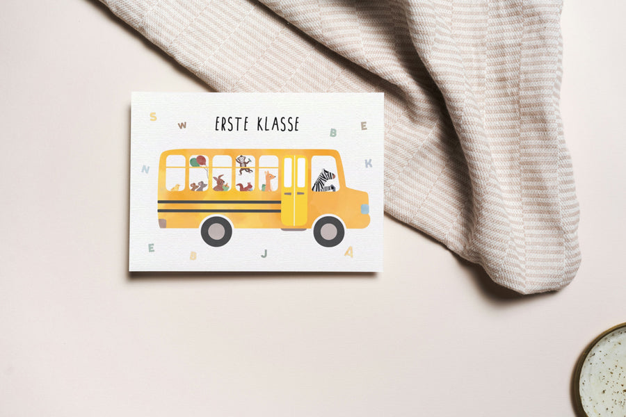 Grußkarte mit der Illustration eines gelben Schulbusses und dem Text „Erste Klasse“ auf hellem Hintergrund