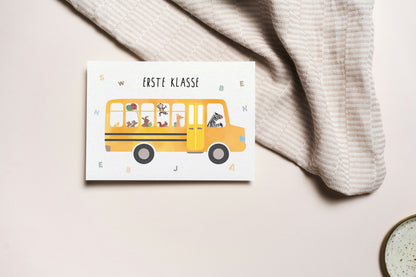 Grußkarte mit der Illustration eines gelben Schulbusses und dem Text „Erste Klasse“ auf hellem Hintergrund
