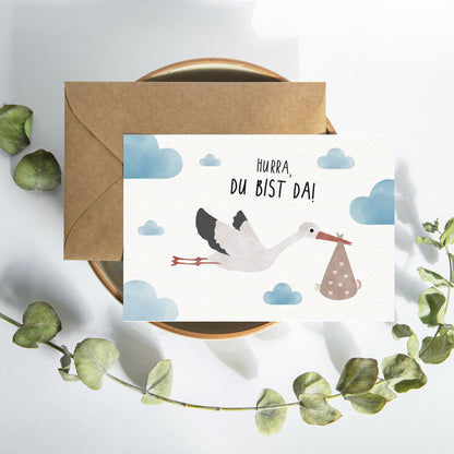 Postkarte mit Storch und dem Schriftzug „Hurra du bist da“ im niedlichen Design, ideal als Geburtskarte oder Willkommensgruß für Babys.