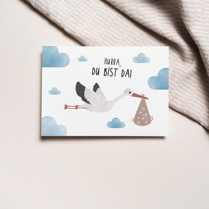 Postkarte mit Storch und dem Schriftzug „Hurra du bist da“ im niedlichen Design, ideal als Geburtskarte oder Willkommensgruß für Babys.